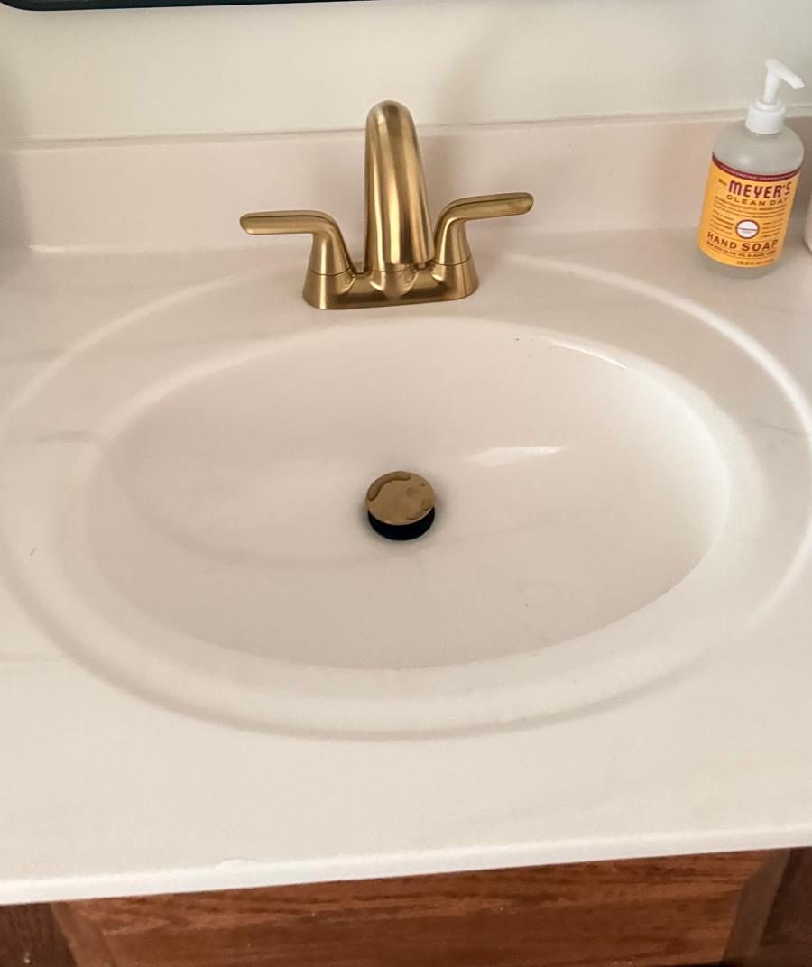 Grifo y desagüe nuevos dorado cepillado en un lavabo de baño