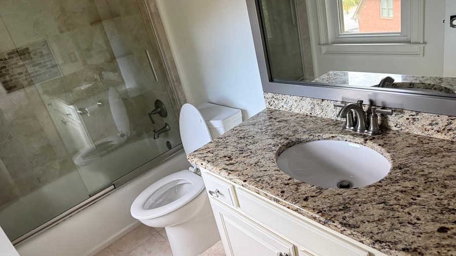 Baño con inodoro, lavabo con encimera de granito y accesorios de tina/ducha